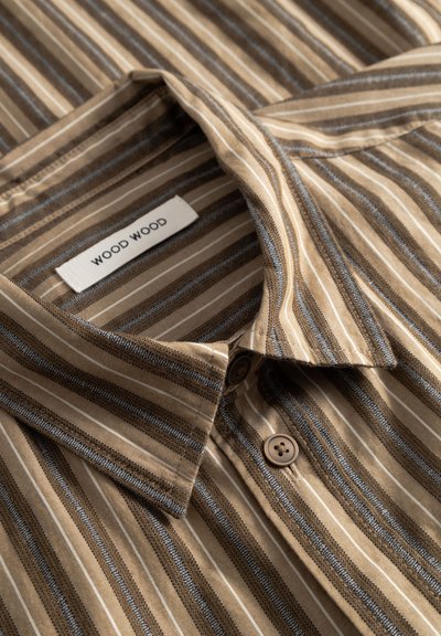 Złożona beżowo-brązowa koszula w paski na guziki z kołnierzykiem i widoczną metką marki "WOOD WOOD" wewnątrz kołnierza.