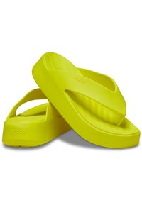 Des tongs en caoutchouc jaune avec une semelle épaisse et un lit de pied texturé. Le design comprend des lanières larges et le logo "crocs" sur le côté.