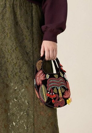 Beaded handbag with a curved shape, featuring multicolored floral patterns, black velvet material, and small handle. Worn with an olive green lace skirt.