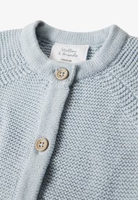 Cardigan lavorato a maglia azzurro chiaro con scollo rotondo, bottoni in legno e motivo testurizzato. L'etichetta riporta "Stellou & Friends," taglia 62/68.