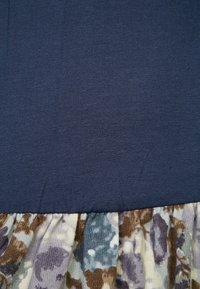 Marineblauwe stof genaaid aan verzamelde rokstof met een bloemmotief in gedempte paarse, bruine en beige tinten.