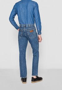 Jeans de mezclilla de corte recto, color azul y costuras en contraste. Presentan una etiqueta de cuero en el bolsillo trasero y rayas laterales.