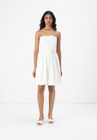 Hvid stramningsløs kjole med et struktureret liv og en samlet skirt. Glat stof med en afslappet pasform, parret med beige slidesandaler.