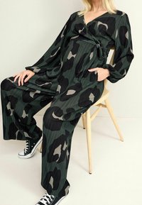 Salopette de maternité noire et vert olive avec un design enroulé, dotée de manches longues, d'une taille cintrée et d'une coupe ample. Tissu texturé avec un motif camouflage.