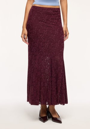 Donna che indossa una gonna lunga in pizzo bordeaux scuro a vita alta abbinata a scarpe con tacco a punta bordeaux dello stesso colore.