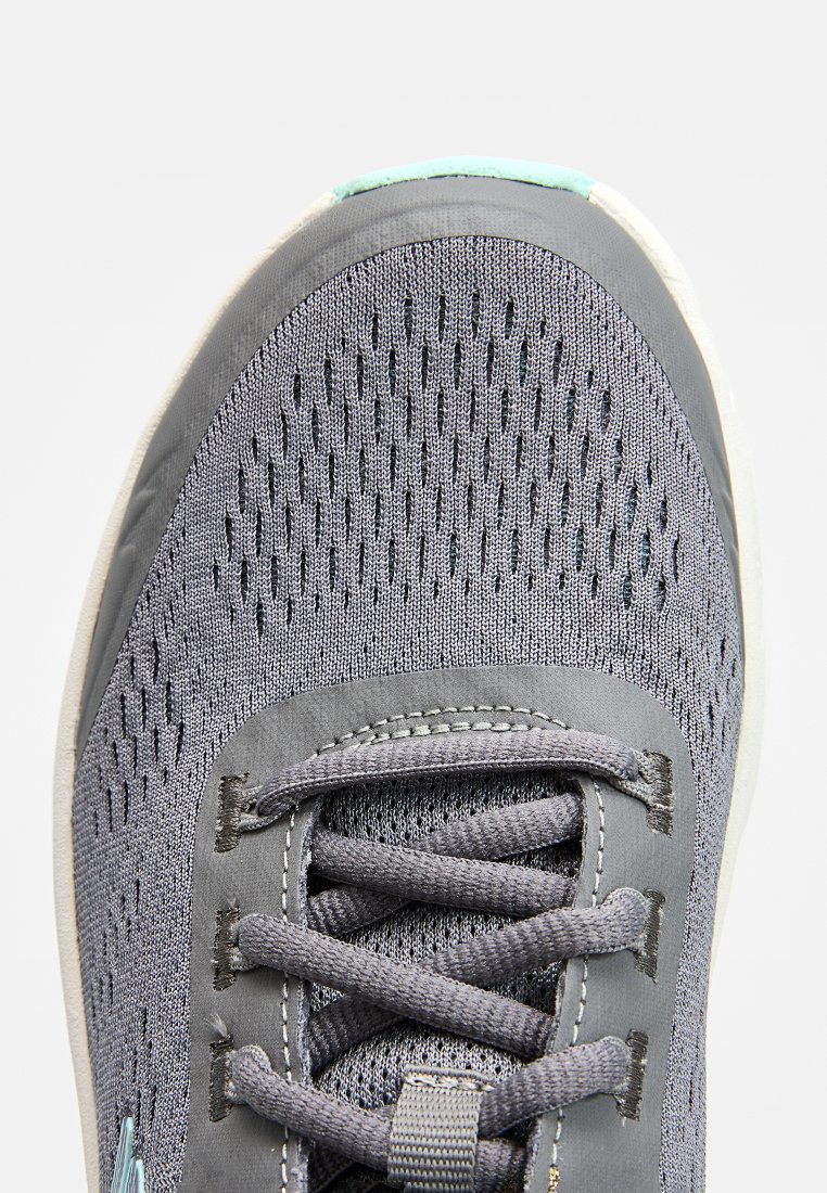 Zapatilla deportiva gris con parte superior de malla que presenta agujeros de ventilación, cordones planos grises y un acento verde claro cerca de la puntera.