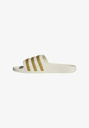 Sandalo slide bianco con suola texturizzata e quattro strisce glitter oro sulla fascia superiore, mostrato di profilo su sfondo bianco.