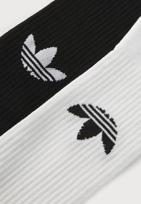 Meias caneladas em preto e branco com um logótipo proeminente de cada lado e detalhes em riscas horizontais pretas na meia branca.