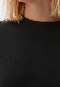 Pull noir en maille avec un col montant. Le tissu semble doux avec une texture lisse et un subtil côtelé le long du col.