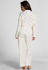 Weißes Schlafanzugset mit floralem Muster, bestehend aus einem Hemd mit Knopfleiste und geraden Hosen. Weicher Stoff mit subtiler Textur und lässiger Passform.