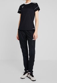 Svart träningskläder inklusive en kortärmad tröja med vita detaljer och svarta byxor, kombinerat med vita och svarta spikskor med snören.