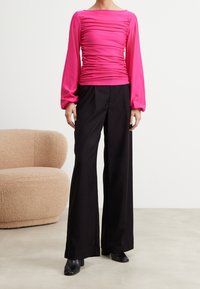 Fuchsiakortärmad topp med rynkad struktur och fyrkantig halsringning, kombinerad med svarta vida byxor och svarta ankelstövlar.