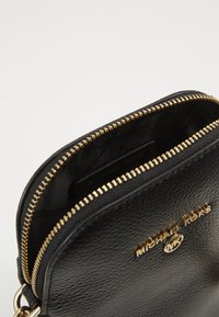 Svart läderhandväska med guldhardware, dragkedjestängning och präglad logotyp. Inuti finns en tygfoder och en ficka för organisering.