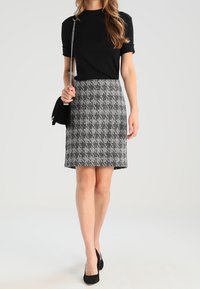 Musta lyhythihainen paita yhdistettynä harmaasävyiseen ja mustaharmaaseen houndstooth-hameeseen. Asustetta täydentää pieni musta käsilaukku ja mustat korkokengät.