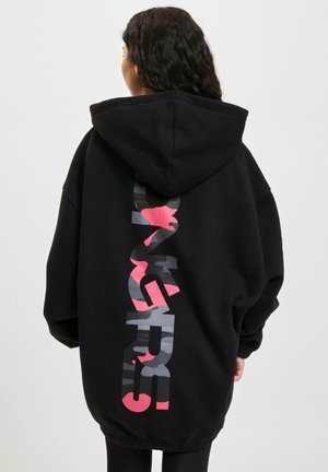Hoodie noir oversize présentant un design graphique réfléchissant dans des nuances de gris et de rose au dos. Comprend une capuche avec cordon de serrage.