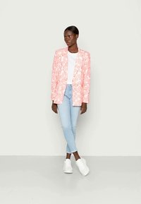 Blazer rosa com padrão floral e design ajustado. Combinado com uma t-shirt branca, jeans azul claro e ténis brancos para um visual casual.