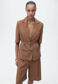 Brun tvådelad outfit bestående av en kortärmad blazer med bälte och shorts, tillverkad av ett texturerat tyg, med knapppdetaljer och fickor.