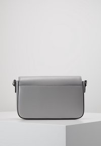 Šedá kožená crossbody taška obdélníkového tvaru, hladké textury a černých akcentů. Obsahuje klopový uzávěr a nastavitelné ramínko.