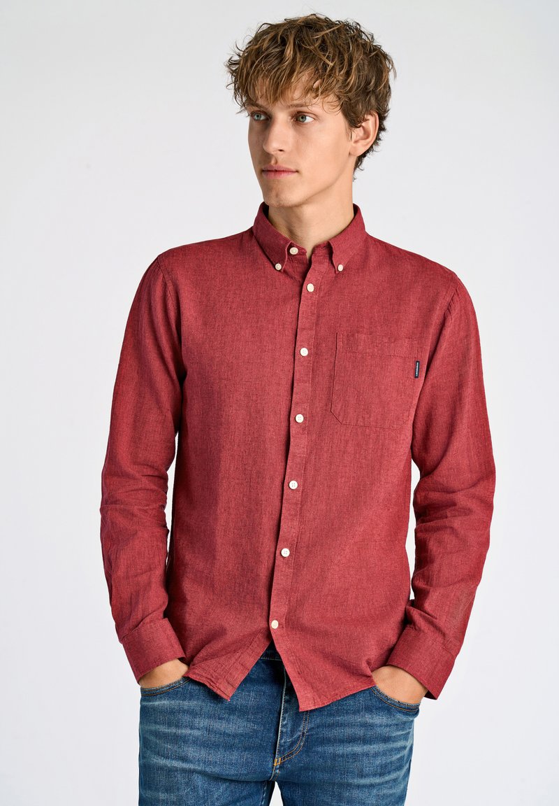 Camicia rossa aperta con bottoni, realizzata in tessuto texturizzato e dotata di taschino frontale. Presenta un colletto classico e bottoni bianchi; abbinata a jeans di denim.