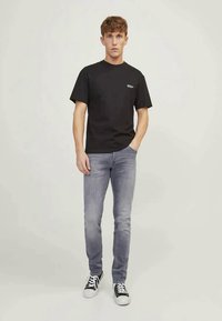 T-shirt de algodão preta com mangas curtas, combinada com jeans cinza claro. O calçado consiste em ténis pretos e brancos. Design minimalista.