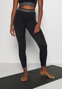 Leggings deportivas negros con un diseño ajustado, textura suave y una cinturilla reflectante plateada. Combinados con un top corto a juego.