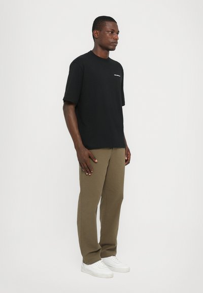 Tricou negru cu mânecă scurtă și guler rotund, purtat cu pantaloni scurți maro deschis și adidași albi. Design simplu, fără modele vizibile.