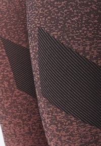 Leggings atléticos con un patrón en rosa y negro. Presentan una tela texturizada con rayas negras diagonales sobre un fondo pixelado.