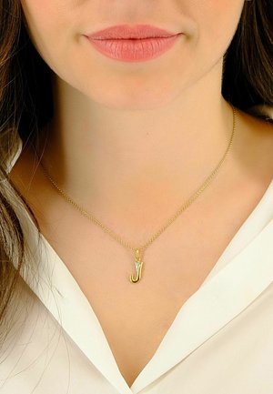 Collier en or avec un pendentif en forme de 'J', orné d'un petit triangle. Le modèle porte une chemise blanche, mettant en valeur le design délicat de la chaîne.