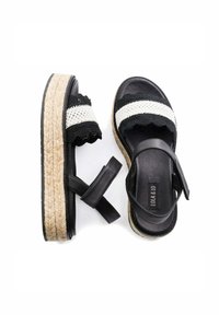 Sandalias espadrilles en blanco y negro con correas de tela trenzada, con una suela gruesa de yute y una suela plana negra. Incluye una correa ajustable para el tobillo.