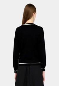 Maglione nero a maglia con maniche lunghe, caratterizzato da rifiniture bianche lungo il collo e l'orlo. Il tessuto sembra morbido con una finitura leggermente strutturata.