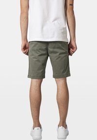 Shorts en coton vert olive avec des ourlets retournés, dotés de poches latérales et arrière, associés à des baskets blanches et un t-shirt blanc unis.