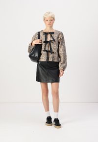 Blusa de estampado animal com laços pretos, combinada com uma saia mini de couro preta. Usando ténis pretos e meias brancas, segurando uma bolsa preta.