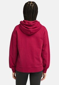 Röd huvtröja med avslappnad passform, ribbade muddar och fåll, samt mjuk textur, sedd bakifrån mot en enhetlig bakgrund.