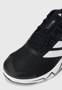 Czarny but sportowy z siateczkową cholewką, białymi akcentami i teksturowaną gumową podeszwą. Posiada zaokrąglony nosek i system sznurowania.