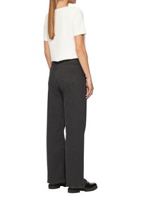 Jean noir à jambes larges avec une taille haute, poches arrière et un tissu lisse et texturé. Associé à un haut blanc à manches courtes.
