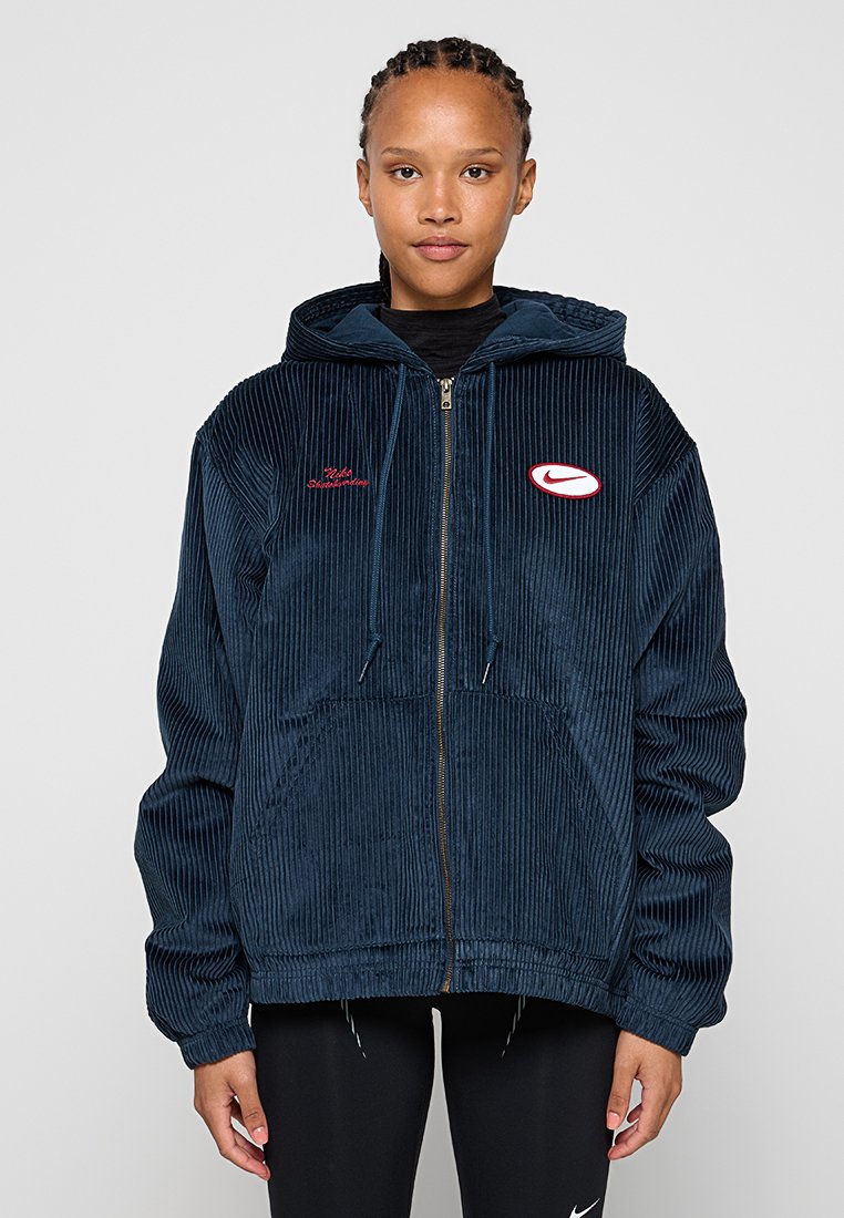 Veste à capuche en velours côtelé marine avec fermeture éclair. Présente un texte rouge brodé et un patch logo blanc. Grandes poches avant et coupe décontractée.