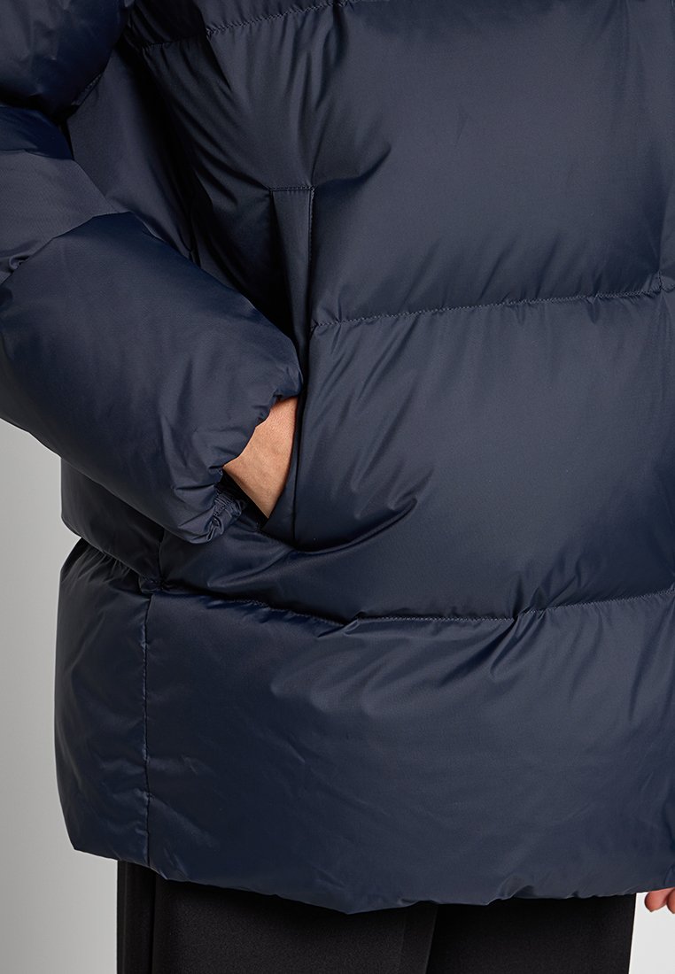 Granatowa kurtka puchowa z pikowanym wzorem, dużym kołnierzem i bocznymi kieszeniami. Gładki, błyszczący materiał o luźnym kroju.