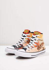 Tenisky s vysokým nadpatkem s grafikou Looney Tunes, převážně oranžové a černé plátno, bílé tkaničky a gumové podrážky s černým lemem.