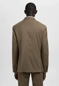 Braune, maßgeschneiderte Anzugjacke mit klarer Silhouette, Kantenrevers und geknöpften Manschetten, Rückansicht vor neutralem Hintergrund.