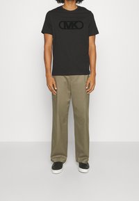 Černé tričko s kulatým výstřihem a sametovým logem MK, spárované se světle olivovými širokými kalhotami a černými teniskami. Minimalistický design, volný střih.