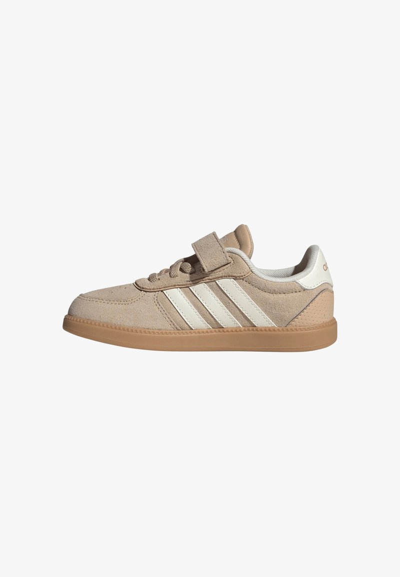 Baskets en daim beige avec trois bandes blanches, semelle en caoutchouc marron clair, lacets et une bride velcro sur le dessus.