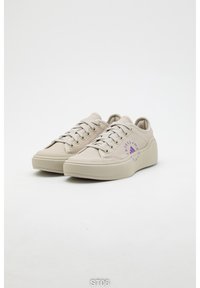 Béžové plátěné tenisky s texturovanou podrážkou, fialovými logy a klasickým šněrováním. Zaoblená špička a polstrovaný límec.