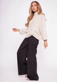Gruby, kremowy sweter o wysokim kołnierzu, w połączeniu z czarnymi spodniami z szerokimi nogawkami, charakteryzującymi się luźnym krojem i miękką teksturą.