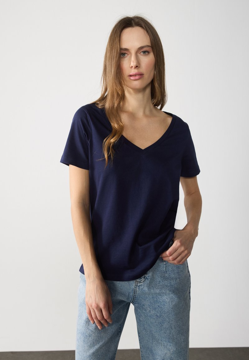 Marinblå bomullströja med V-hals, korta ärmar och avslappnad passform, i kombination med ljusblå denimjeans. Enkelt och minimalistiskt design.