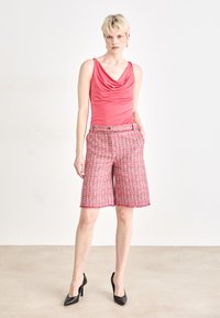 Rosa top mit Kapuze, kombiniert mit knielangen rosafarbenen Tweed-Shorts mit fransigem Saum und seitlichen Taschen, getragen mit schwarzen High Heels.