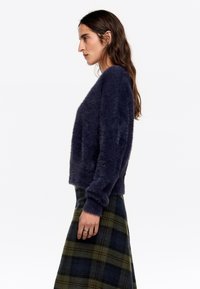 Granatowy, puszysty sweter z długimi rękawami, połączony z zieloną i granatową, kraciastą spódnicą, charakteryzującą się miękką teksturą i luźnym krojem.