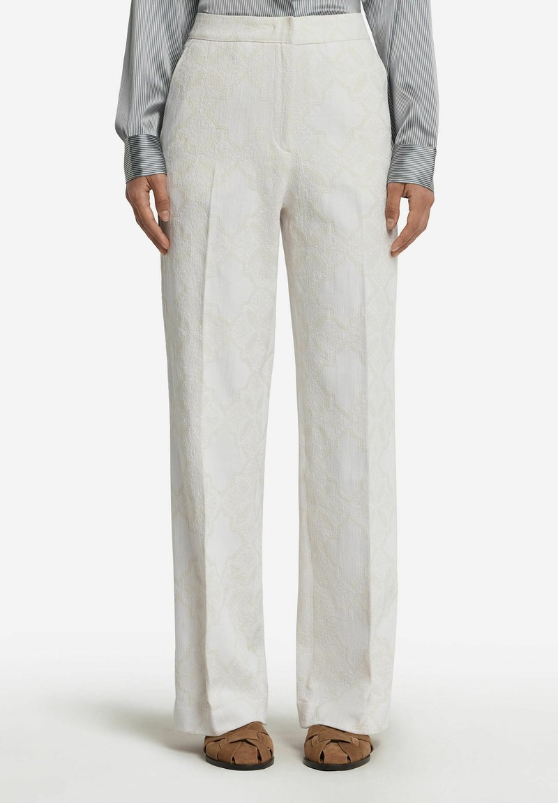 Pantalons blancs structurés présentant un motif géométrique texturé, avec une taille haute et une coupe droite. Associés à des chaussure slip-on couleur tan.
