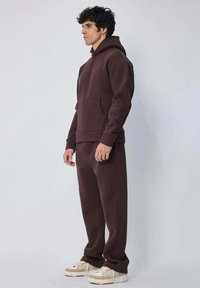 Hoodie bordeaux avec poche kangourou, assorti à un pantalon de jogging bordeaux. Présente des poignets et un ourlet à côtes, porté avec des baskets beiges.
