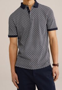 Námořnická polo košile se vzorovanou tkaninou, která obsahuje geometrické tvary v světle modré a bílé barvě. Krátké rukávy s kontrastním límečkem a manžetami.