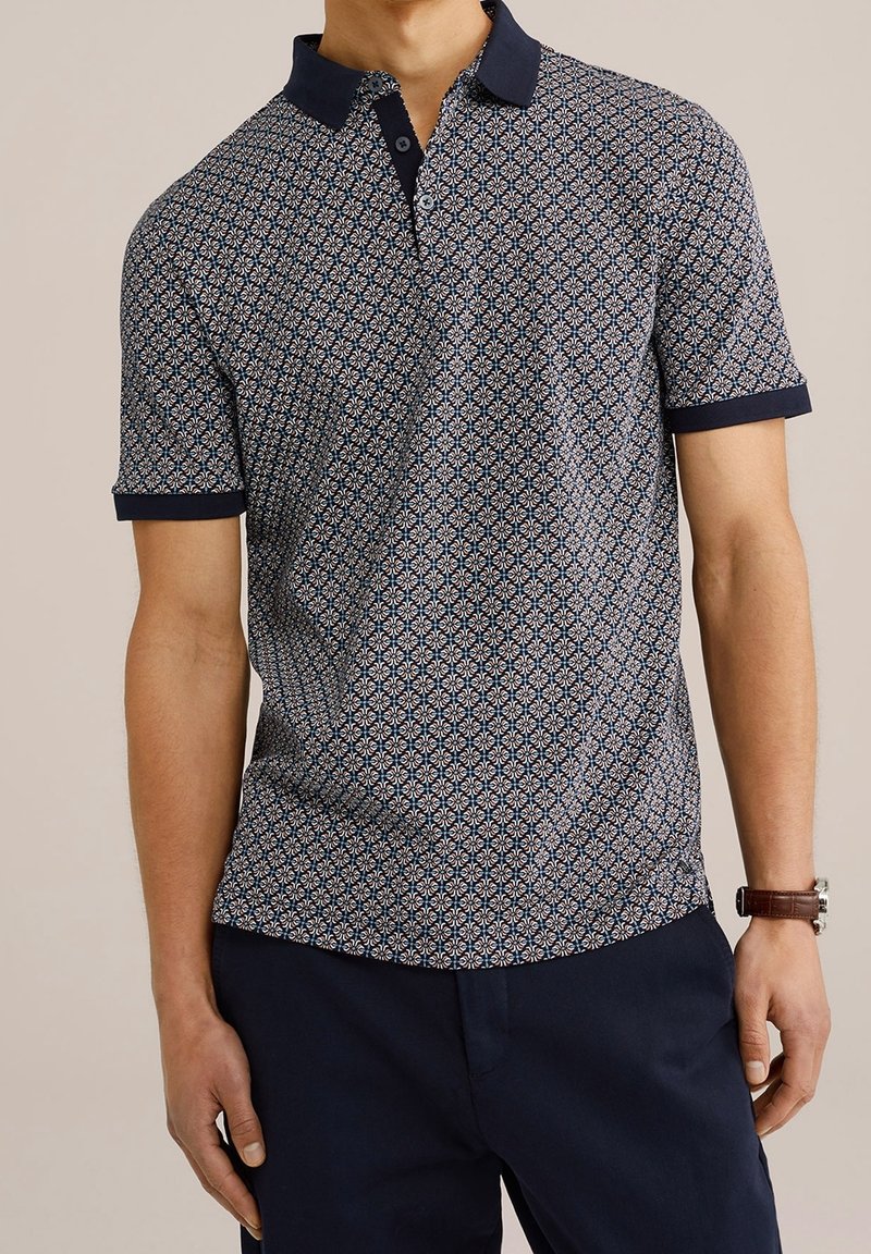 Námořnická polo košile se vzorovanou tkaninou, která obsahuje geometrické tvary v světle modré a bílé barvě. Krátké rukávy s kontrastním límečkem a manžetami.